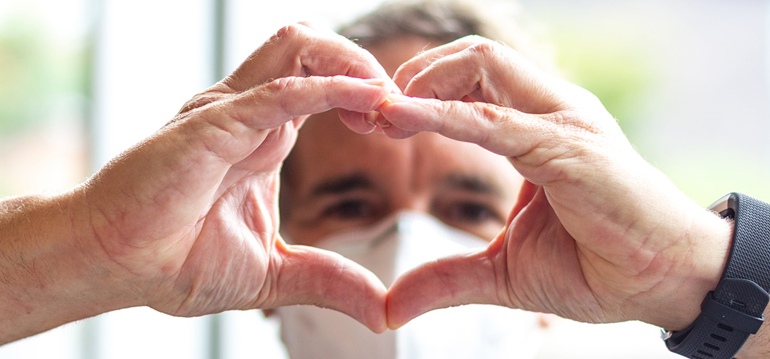 Two hands forming a heart with a blurred face in the background