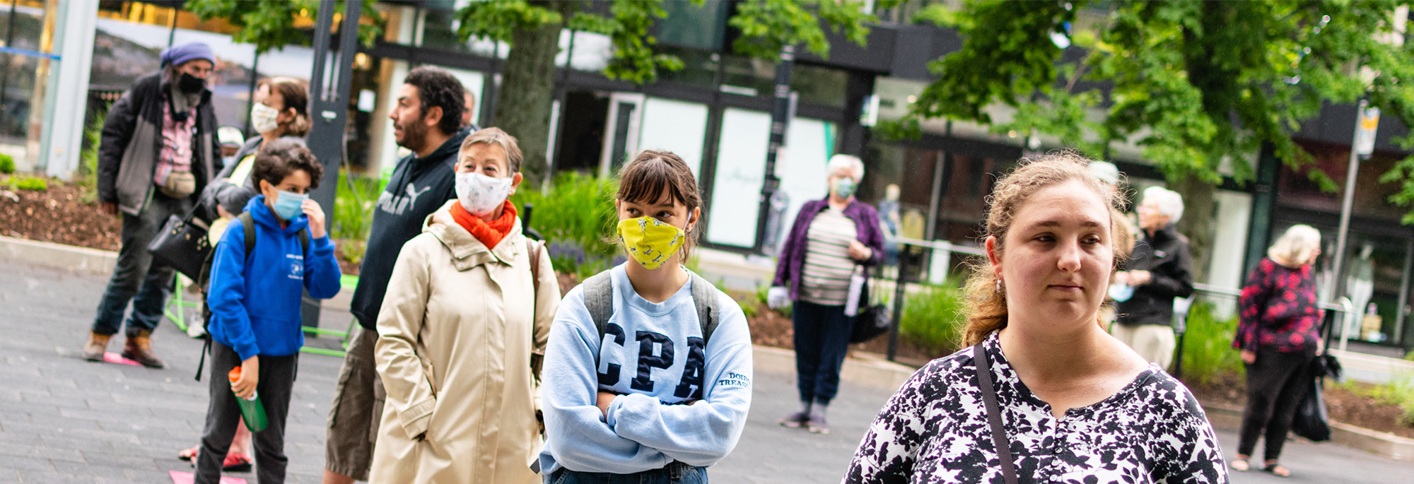 Several people wearing masks stand in line for curbside pick-up at the Halifax Central Library