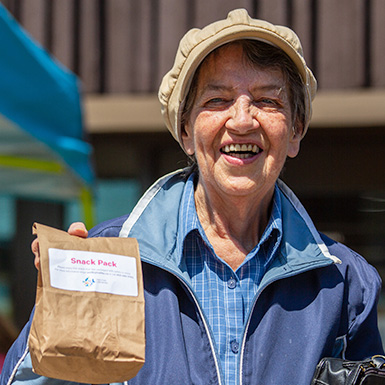 A senior citizen smiling and holding up a Grab and Go snack pack